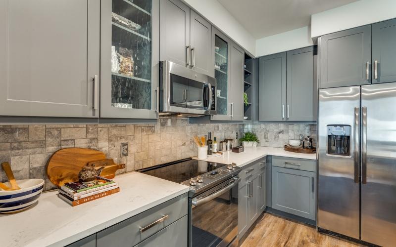 a kitchen with grey cabinets a fridge and a stovetop